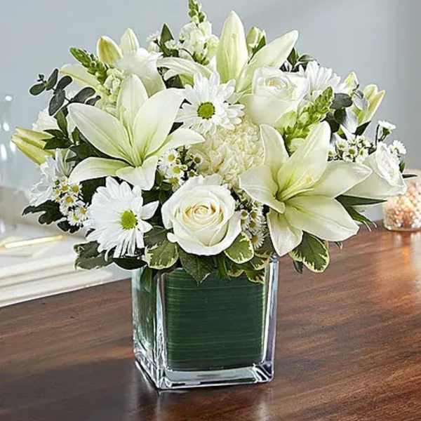 White lilies and roses arranged in a square glass vase
