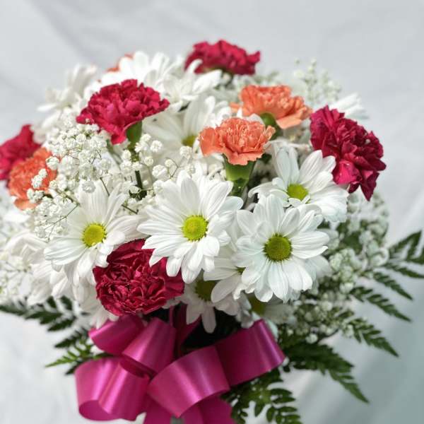 Bouquet of white daisies and pink carnations with a magenta ribbon in a vase