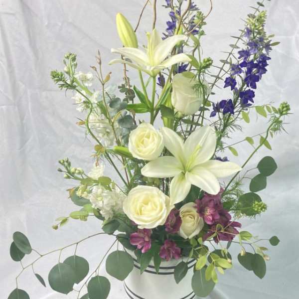 Tall white lily and rose arrangement with purple accents in a striped vase
