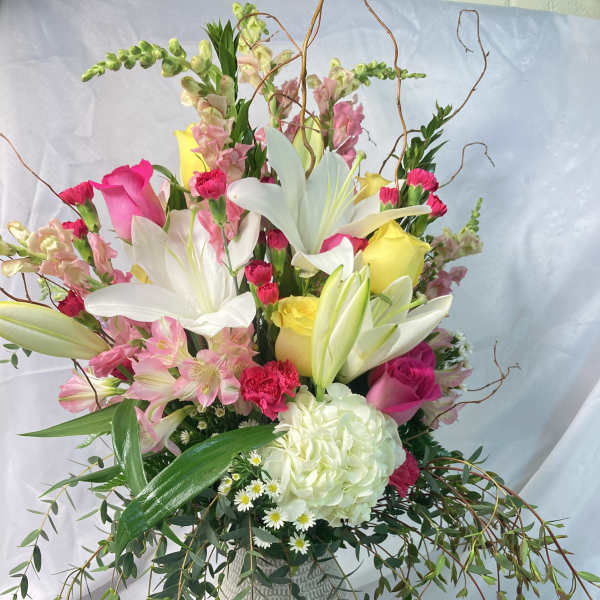 Tall mixed bouquet in a white vase with lilies, roses, and pink blooms