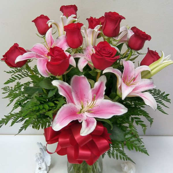 Bouquet of red roses and pink lilies in a glass vase with a red ribbon