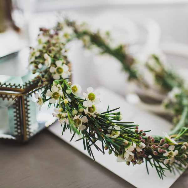 Floral crown with small white blossoms and green sprigs beside a glass lantern