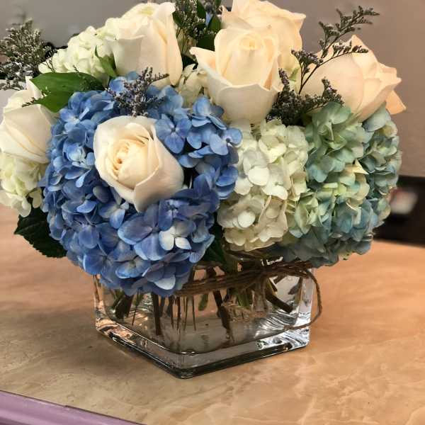 Blue and white hydrangeas with cream roses in a square glass vase