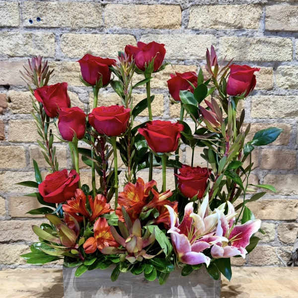 Red roses and pink lilies arranged in a wooden box