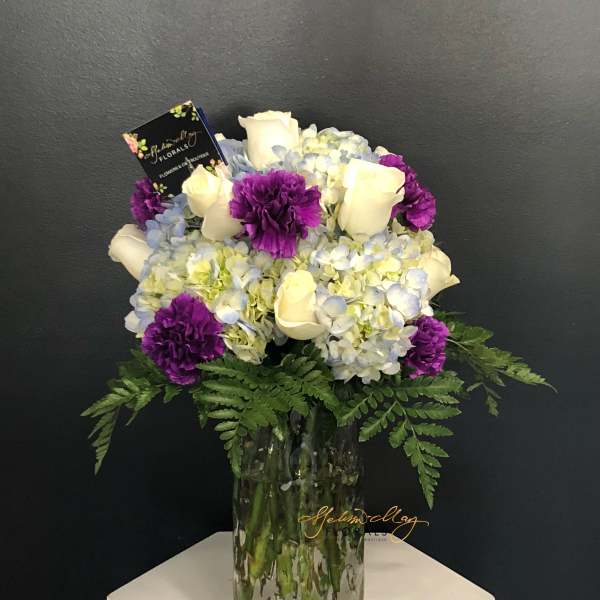 Bouquet of white roses, blue hydrangeas, and purple carnations in a glass vase