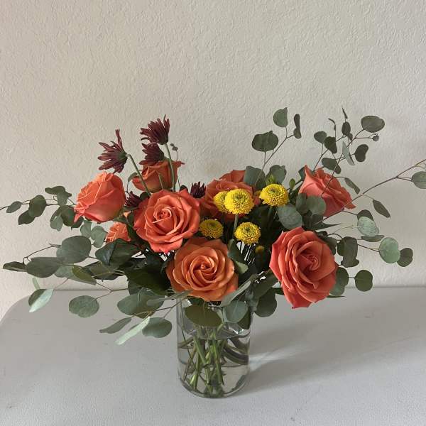Orange roses and yellow button mums in a clear glass vase