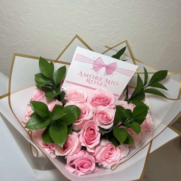 Bouquet of pink roses wrapped in white paper with green leaves