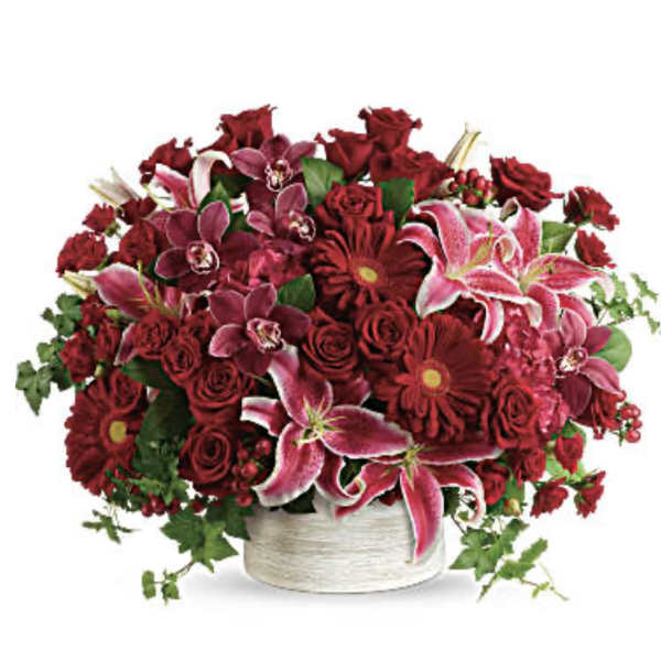 Red and pink mixed flower arrangement in a white container