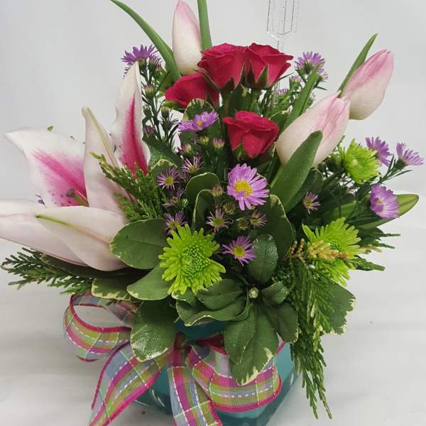 Pink tulips and red roses in a teal vase with a plaid ribbon