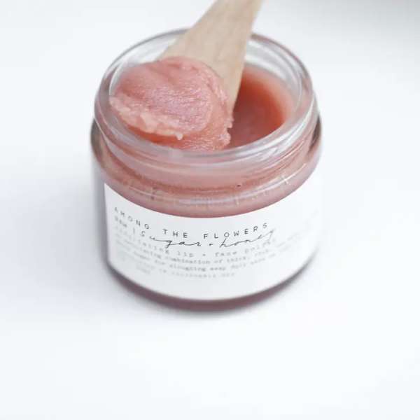Open jar of pink scrub with a wooden spoon