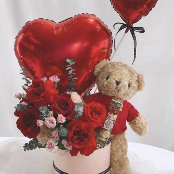 Red heart balloons with roses and a teddy bear in a pink box