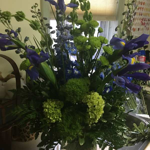Blue iris and green flowers in a clear glass vase