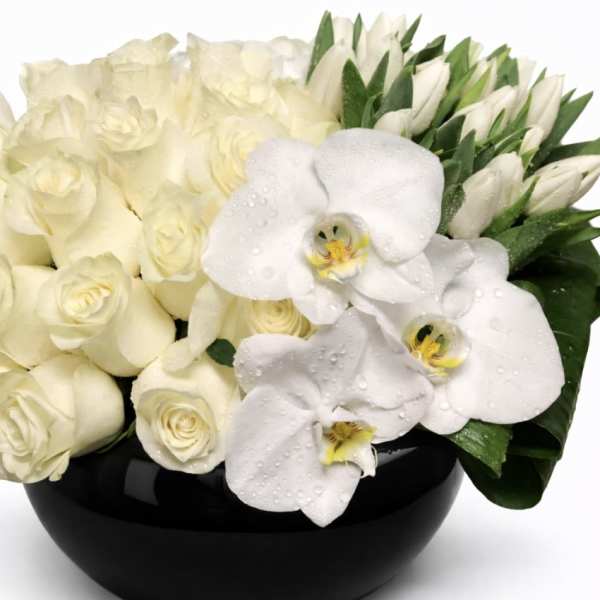 White roses and orchids arranged in a black bowl vase