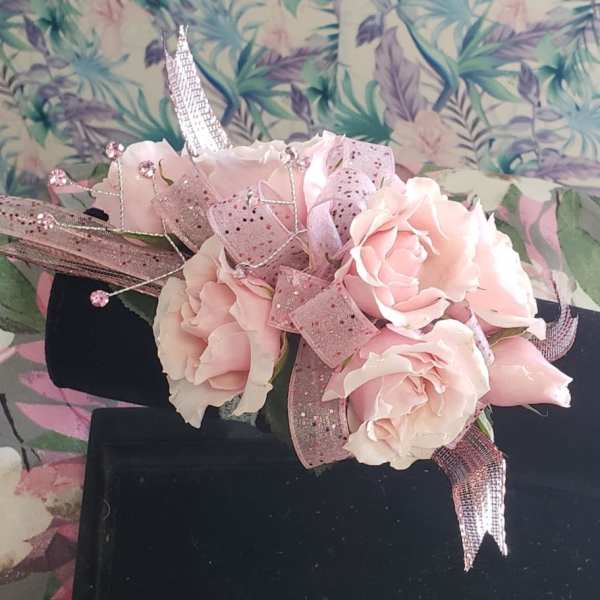 Pink rose corsage with glittery ribbon on a black display stand
