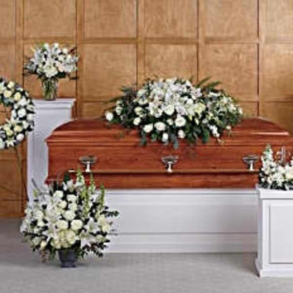 White funeral casket surrounded by white floral sprays and wreaths