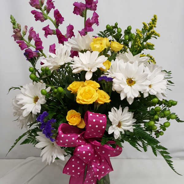 Bouquet of white daisies, yellow roses, and purple snapdragons in a glass vase