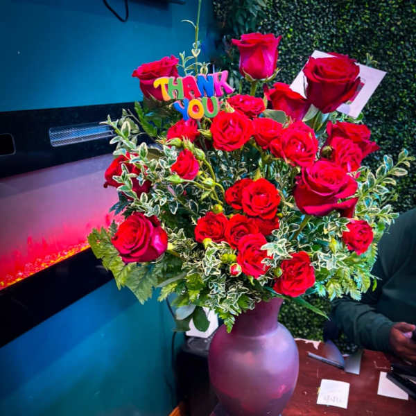 Bouquet of red roses in a purple vase with a colorful "THANK YOU" sign