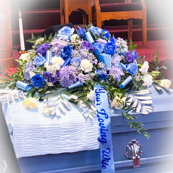 Blue and white floral casket spray with ribbon on a coffin