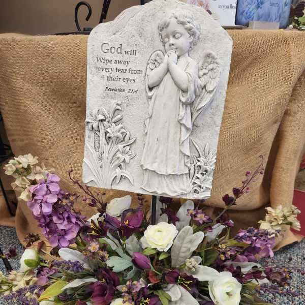 Memorial plaque with angel relief above a purple and white floral arrangement