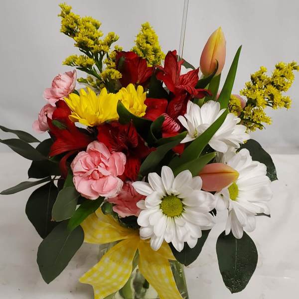Mixed bouquet in a glass vase with daisies, tulips, carnations, and red blooms