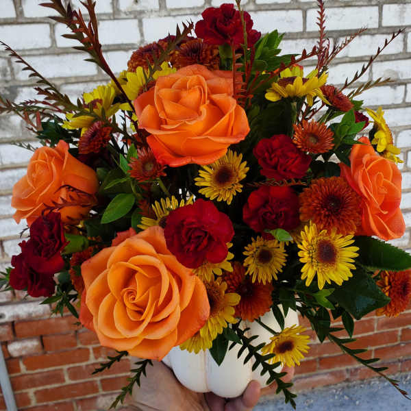 Bouquet of orange and red roses with yellow daisies in a white vase