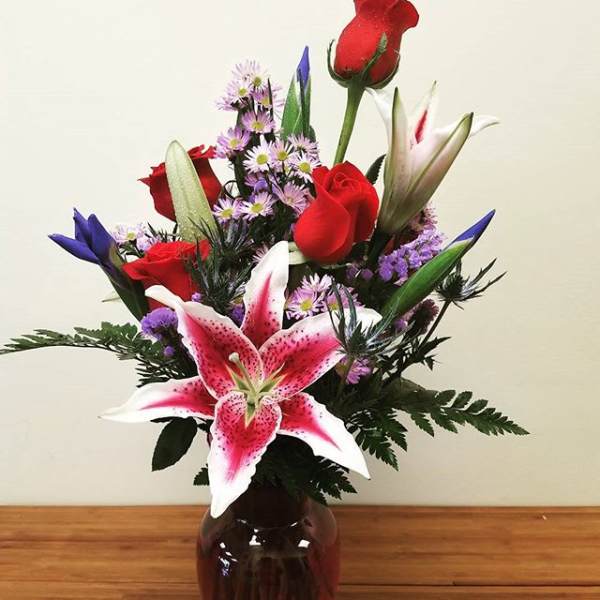 Bouquet of red roses, pink lilies, and purple filler in a dark vase