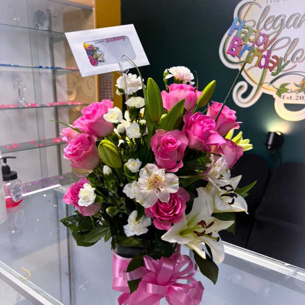 Pink roses and white lilies arranged in a vase with a birthday topper
