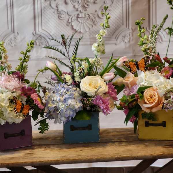 Three floral arrangements in colorful wooden boxes with butterfly accents
