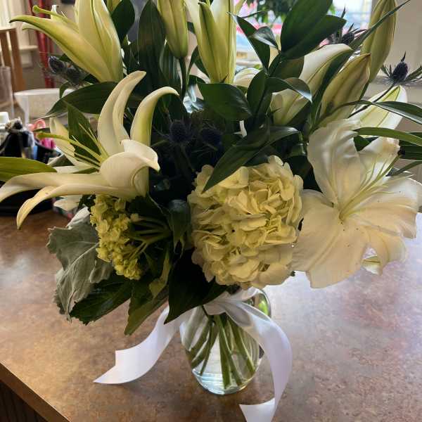White lilies and pale hydrangeas in a glass vase with a white ribbon