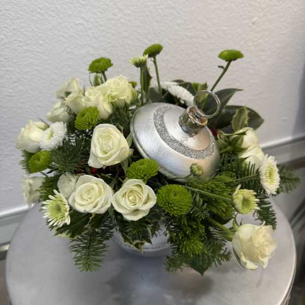 White roses and green button mums arranged around a silver ornament