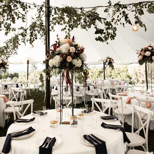 Wedding reception tables under a tent with floral centerpieces and hanging greenery