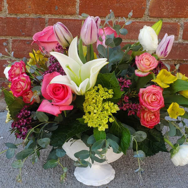 Mixed bouquet in a white pedestal vase with pink roses and white lilies