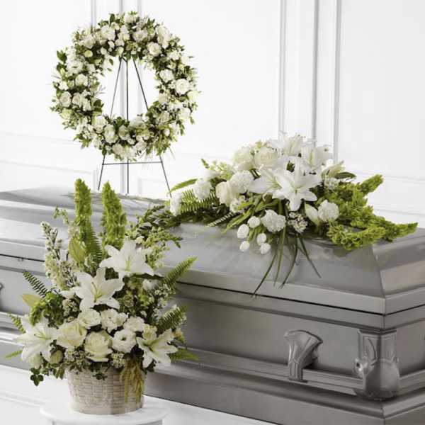 White funeral flowers arranged on a casket with a matching wreath and basket spray.