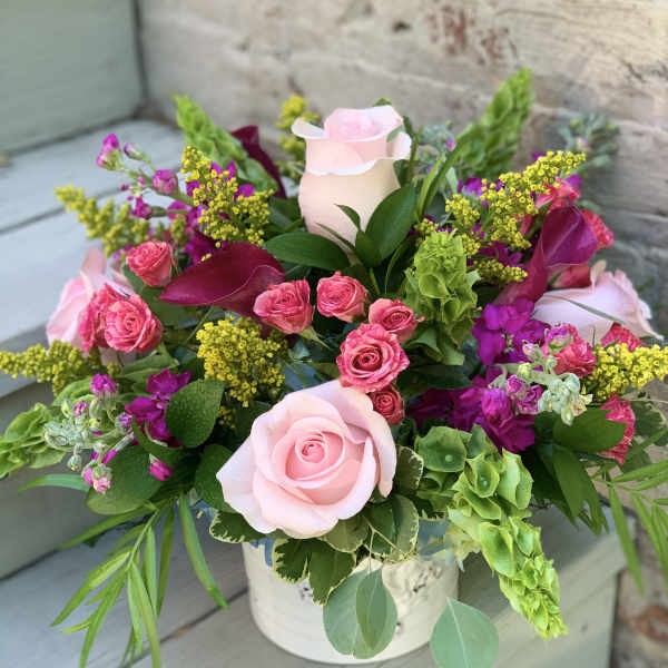 Pink roses and magenta flowers arranged in a white container