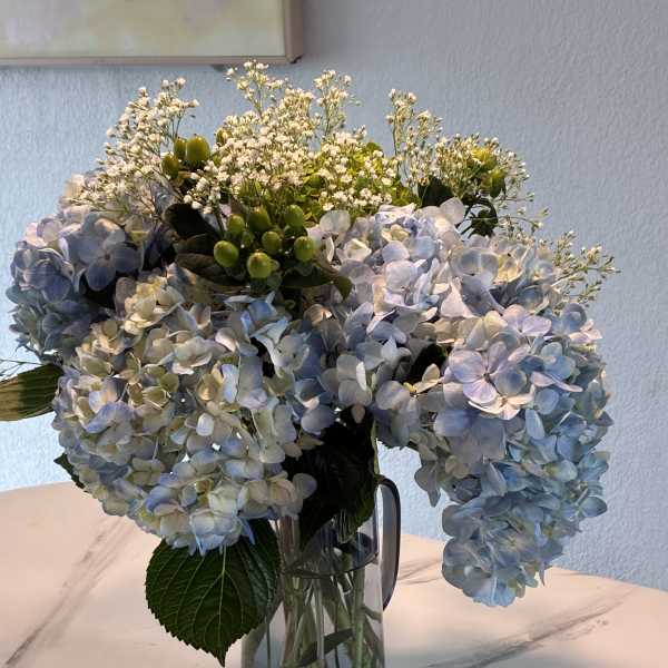 Blue hydrangea bouquet in a glass pitcher vase