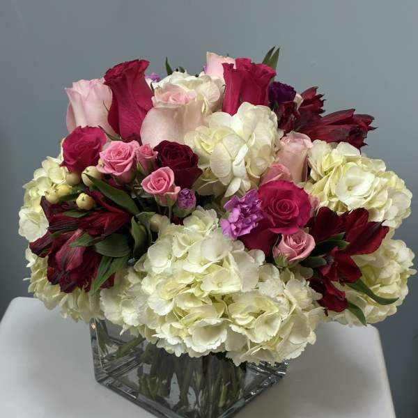 Mixed pink, red, and white flowers arranged in a square glass vase