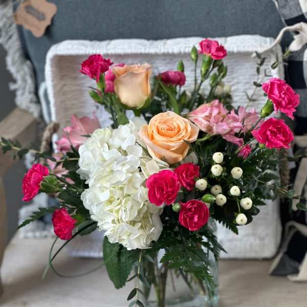 Mixed bouquet of peach roses, white hydrangea, and pink carnations in a glass vase