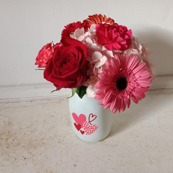 Pink and red flower arrangement in a white heart-decorated vase