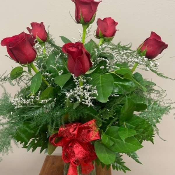 Red roses arranged in a glass vase with a red ribbon