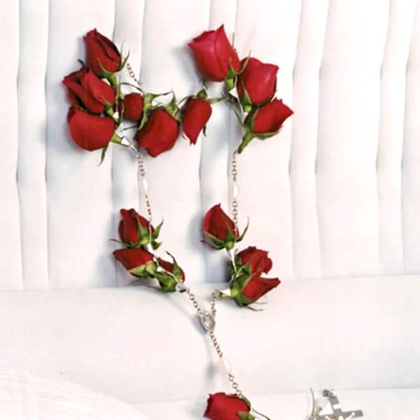 Red rose rosary with silver cross on white fabric