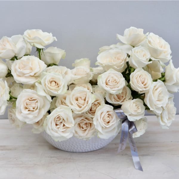 Cream rose arrangement in a white textured bowl with a ribbon bow