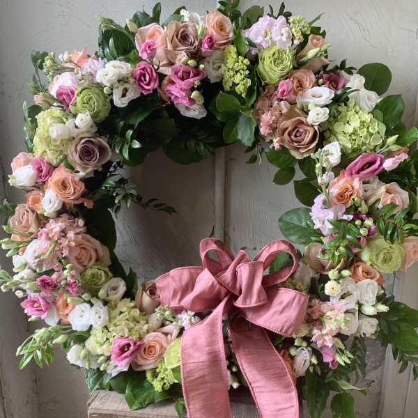 Heart-shaped floral wreath with pink, peach, white, and green blooms and a pink ribbon
