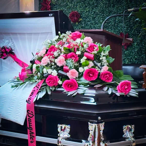 Pink rose and carnation casket spray with ribbon on a black casket