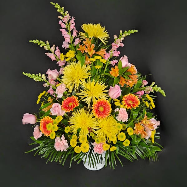 Tall fan-shaped arrangement of yellow and orange blooms with pink accents in a white container