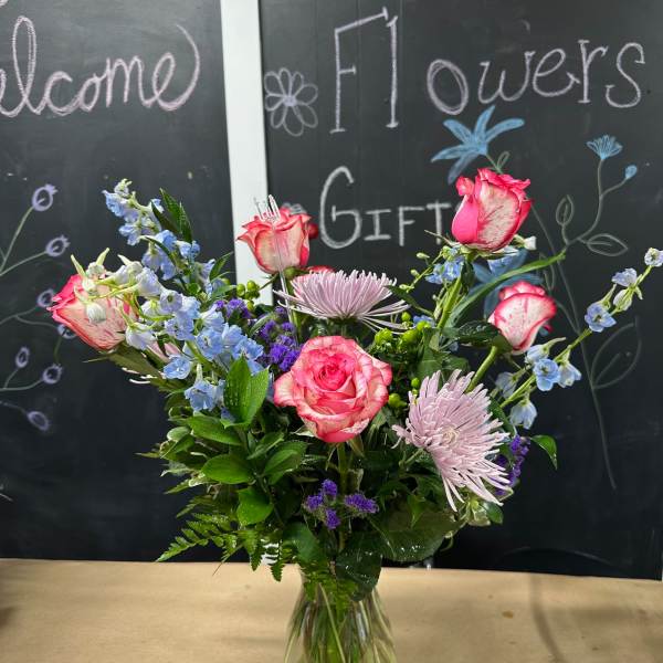 Mixed pink and blue flowers arranged in a clear glass vase