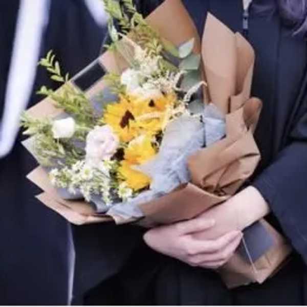 Handheld bouquet of yellow and white flowers wrapped in brown paper