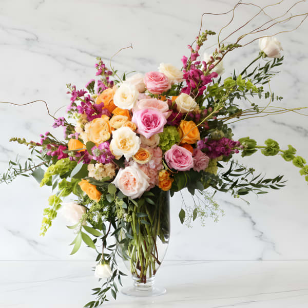 Large mixed bouquet of pink, peach, white, and yellow flowers in a clear glass vase