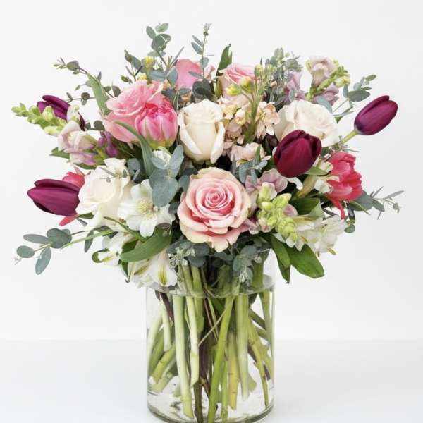 Mixed bouquet of pink, white, and burgundy flowers in a clear glass vase