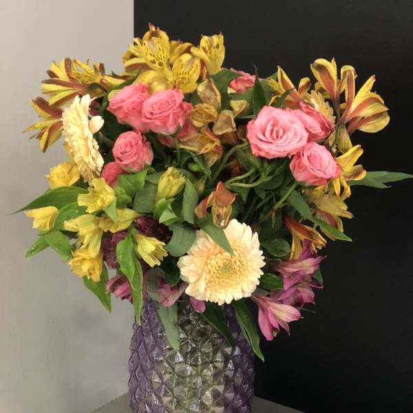Mixed bouquet of pink roses and yellow alstroemeria in a purple glass vase