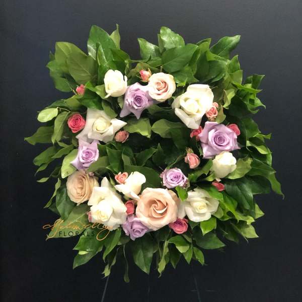 Circular wreath of pastel roses and greenery on a dark stand